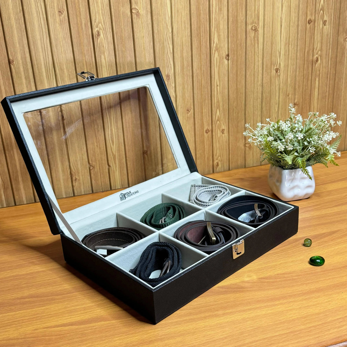 Six-slot belt storage box open on a wooden table with six rolled leather belts in different colours